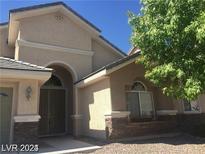 Beige two-story home featuring arched entryway, neutral tones, rock accents, and drought-resistant landscaping at 6245 Hawthorn Woods Ave, Las Vegas, NV 89130