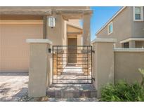 Front gate entry to a two-story home with beige stucco and a paver walkway leading to the front door at 920 Cirrus Cloud Ave, Las Vegas, NV 89138
