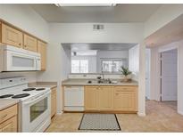 Well-lit kitchen featuring appliances, light wood cabinets, and a pass-through to the living area at 6955 N Durango Dr # 1093, Las Vegas, NV 89149