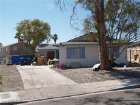 Exterior shot of a single-story home featuring light siding and a large front yard with mature trees and a cracked driveway at 5068 Killarney St, Las Vegas, NV 89122