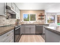 Bright kitchen features gray cabinets, stainless appliances, tile backsplash, and a large window overlooking the yard at 5381 Waving Sage Dr, Las Vegas, NV 89149