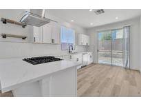 Bright kitchen features stainless hood, white cabinets, island with cooktop, quartz countertops, and access to the backyard at 8944 W Rochelle Ave, Las Vegas, NV 89147