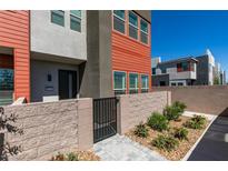 Modern townhouse with red and gray facade, gated entry, and manicured landscaping on a sunny day at 9844 Kings Glen St, Las Vegas, NV 89141