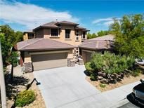 Tan two-story home featuring a two-car garage, stone accents, and tile roof, set against a blue sky backdrop at 5568 Table Top Ln, Las Vegas, NV 89135