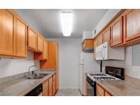 Galley kitchen features wood cabinetry, granite countertops, and modern appliances at 3318 N Decatur Blvd # 2103, Las Vegas, NV 89130