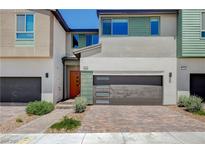 Modern two-story home with a gray garage door, a brick driveway, and colorful front door at 3358 Via Strada St, Henderson, NV 89044