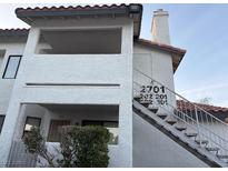 Exterior shot of a white two-story condo with stairs, a red tile roof and a small bush out front at 2701 Beaver Creek Ct # 201, Las Vegas, NV 89117