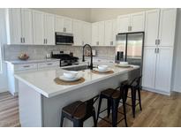 Bright kitchen features white cabinetry, stainless steel appliances, and a quartz countertop island with seating at 5600 Nimes Ave, Las Vegas, NV 89141