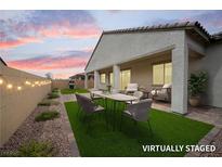 Staged covered back patio with artificial grass, string lights, and dining and seating furniture at 717 Monroe Hill Pl, Henderson, NV 89011