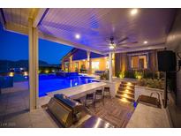 Beautiful outdoor kitchen with tile floors, bar seating, grill and a pool in the background at twilight at 11248 Rebel Dome Ct, Las Vegas, NV 89141