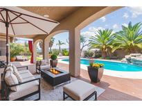 Inviting covered patio with a fire pit and views of the pool and lush landscaping at 7794 River Mist Ct, Las Vegas, NV 89113