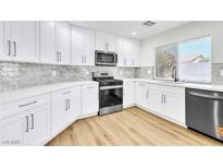 Modern kitchen featuring stainless steel appliances, white cabinets, and light granite countertops and wood-look vinyl flooring at 2112 Hollow Oak Ave, North Las Vegas, NV 89031